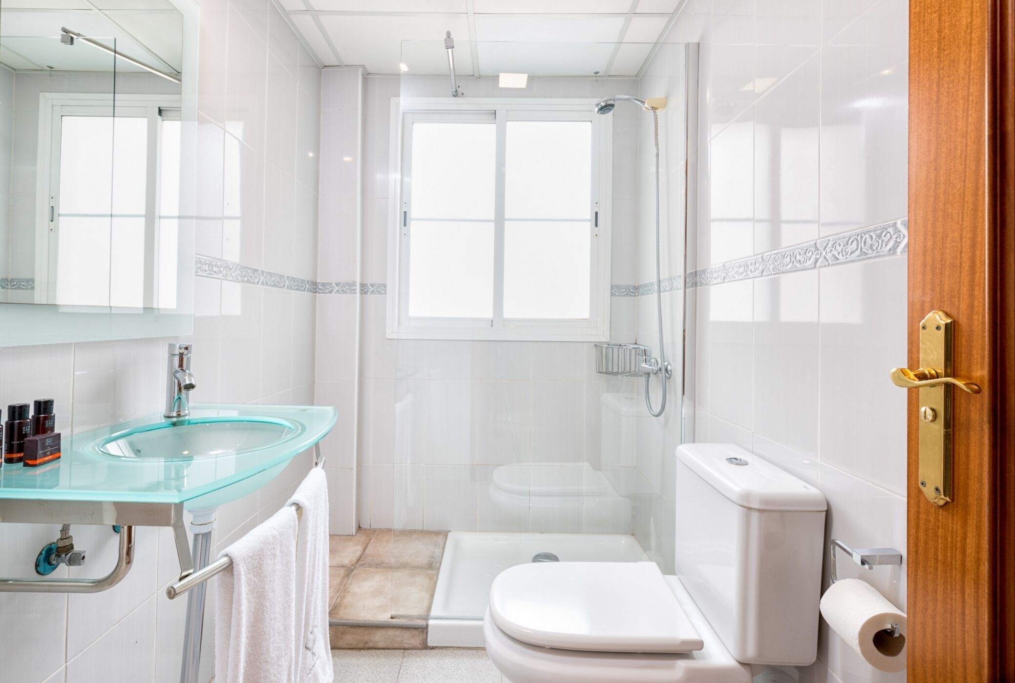 Een moderne badkamer met een glazen wastafel, toilet en douche.