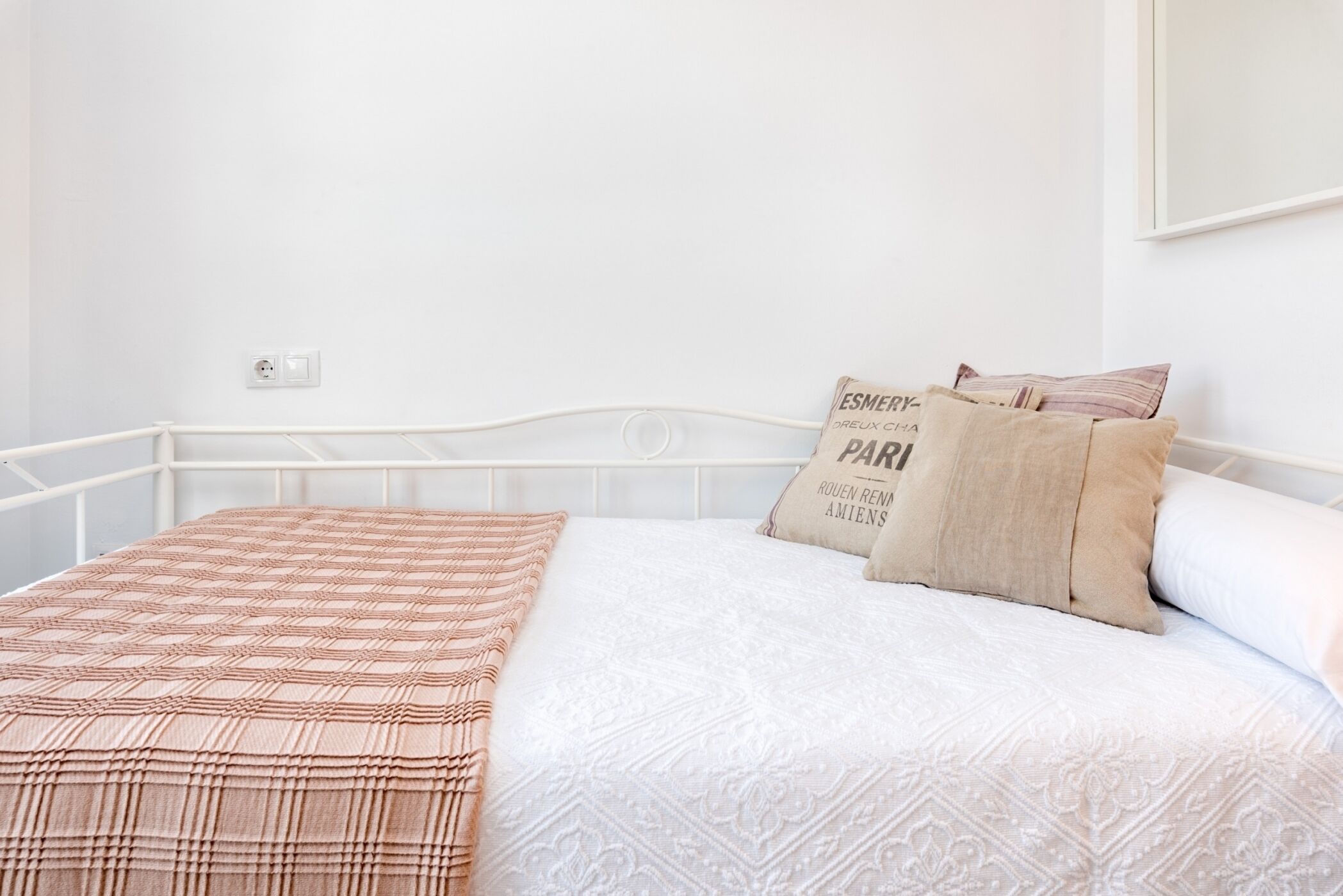 Un lit bien fait, avec une couverture à motifs et deux oreillers, une tête de lit blanche et une prise électrique au mur.