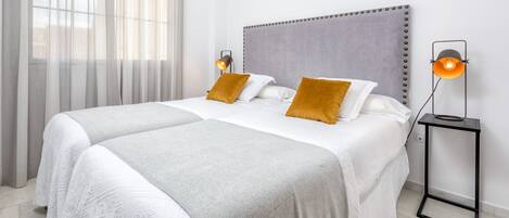 Un letto matrimoniale con una testiera grigia, biancheria da letto bianca e due cuscini color senape. Sono presenti due abat-jour su basi nere.