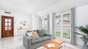 Un salon moderne avec un canapé gris, une table basse en bois et une vue sur un jardin verdoyant, visible à travers de grandes fenêtres.