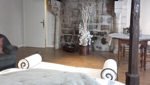 A rustic room with exposed stone walls, a fireplace, a wooden table, and a cozy seating area with a cushioned bench.