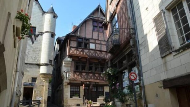 A narrow street with a building featuring a tower and a Tudor-style facade.