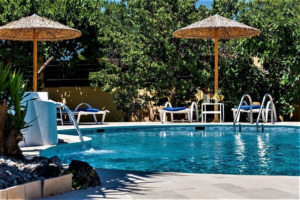 A pool area with two umbrellas, lounge chairs, and a small table with drinks.
