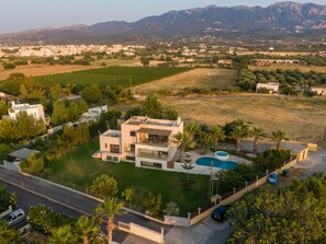 Una casa moderna de dos pisos con piscina, rodeada de un césped cuidado y palmeras.