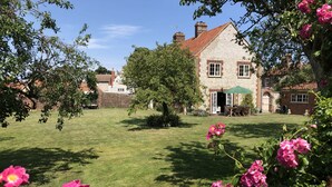 A stone house with a garden, a lawn, and a patio area with outdoor furniture. - 2 Dix Cottages, Thornham, Norfolk (Thornham)