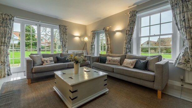 A living room with two grey sofas, a white coffee table, and large windows with curtains. - 2 Dix Cottages, Thornham, Norfolk (Thornham)