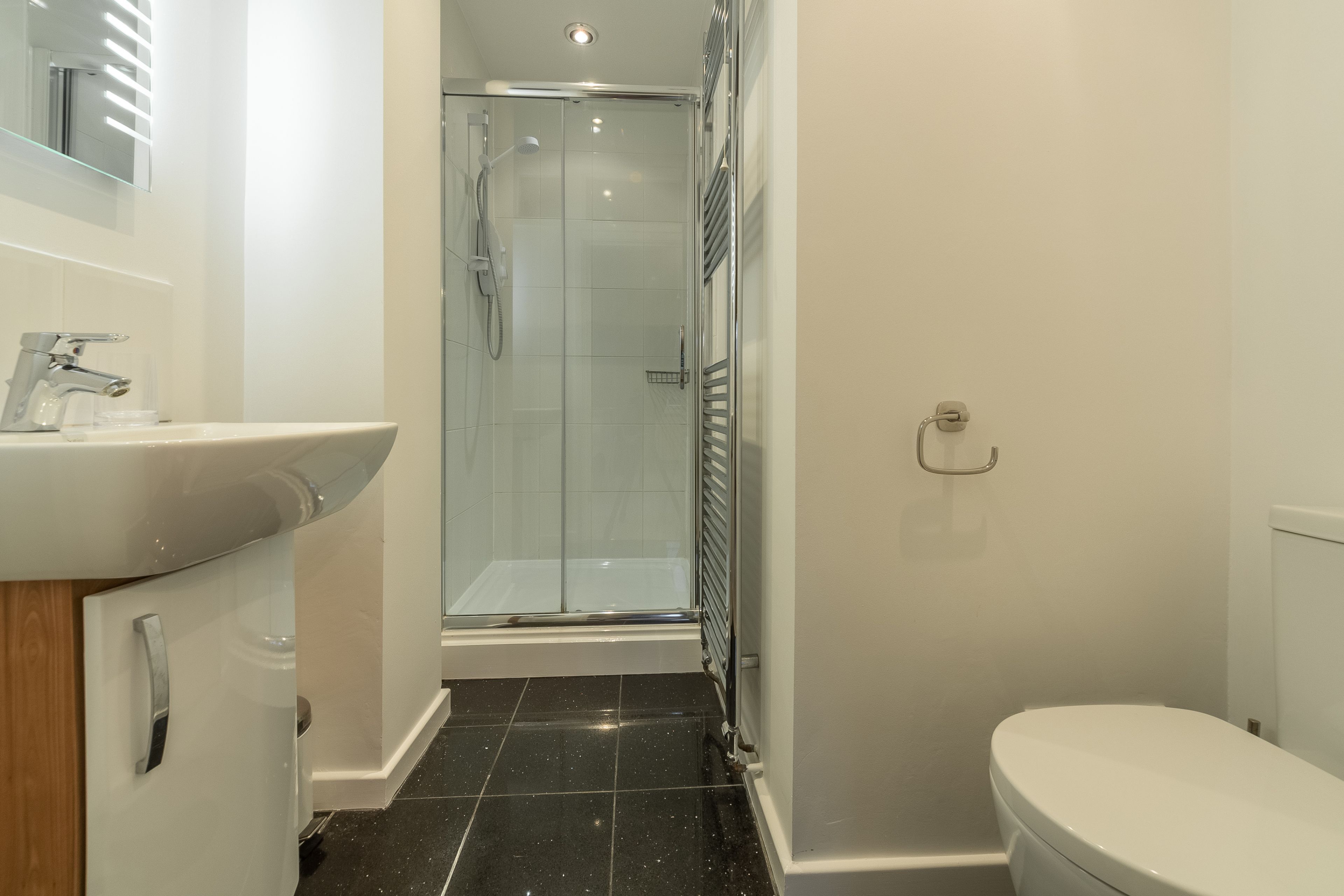 Een moderne badkamer met een douchecabine van glas, een witte wastafel en een toilet.