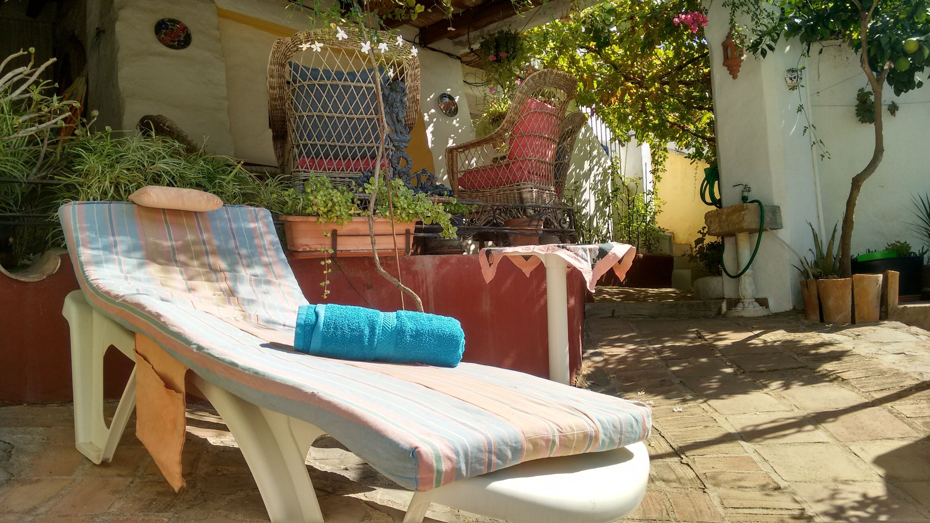 Une chaise longue avec un coussin rayé et une serviette bleue, entourée de plantes en pot et d'une chaise en osier.
