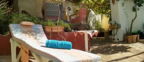 Une chaise longue avec un coussin rayé et une serviette bleue, entourée de plantes en pot et d'une chaise en osier.