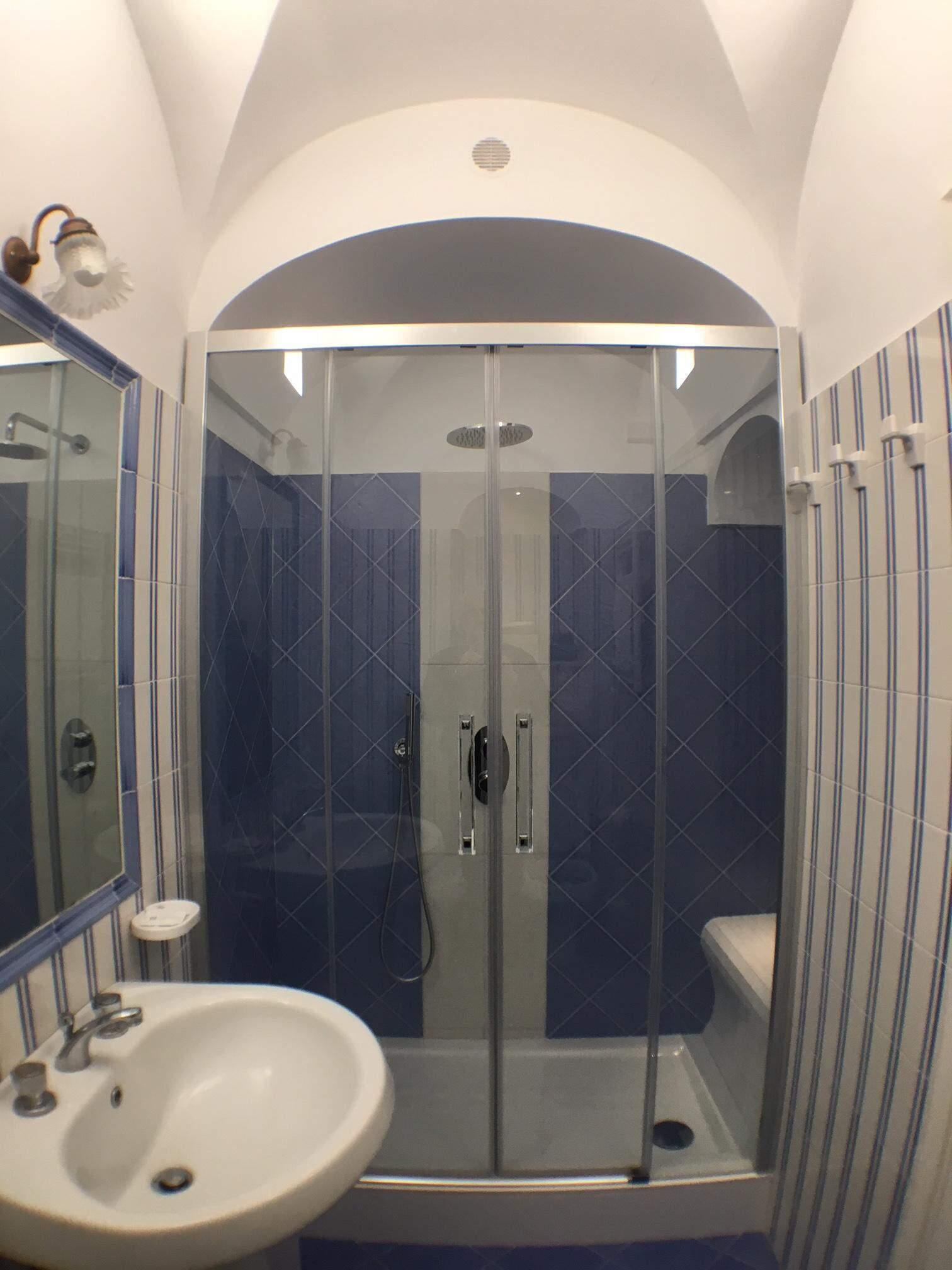 A modern bathroom with a glass-enclosed shower, a white sink, and blue-tiled walls.