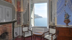 A room with a large window overlooking a body of water, a fireplace, and two chairs. - Amalfi Coast - Il Monaco, Three Bedrooms villa with equipped platform on the sea (Ravello)