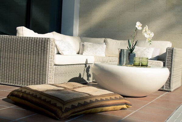 A wicker sofa with cushions, a white coffee table, and a patterned pillow on a tiled floor.