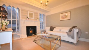 A living room with a fireplace, white sofa, glass coffee table, and a chandelier. - Spacious, detached & private Lakeland hideaway near Cark / Cartmel (Cumbria)