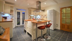 A modern kitchen with white cabinets, a central island with stools, a built-in oven, and a refrigerator. - Spacious, detached & private Lakeland hideaway near Cark / Cartmel (Cumbria)