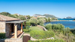 Une propriété située sur la côte, dotée d’un bâtiment en pierre, d’une terrasse et offrant une vue sur la mer et les montagnes.