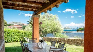 Un espace extérieur aménagé pour les repas, avec une table et des chaises, un mur en pierre et une vue sur un lac et des montagnes.