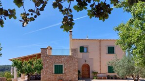 A stone building with a wooden door and green shutters, surrounded by gravel and trees. - Country villa with pool, private garden and barbecue near the beach OFFER June (Manacor)