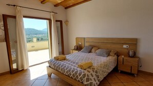 A bedroom with a wooden bed, a nightstand, and a view of the outdoors through a sliding door. - Country villa with pool, private garden and barbecue near the beach OFFER June (Manacor)