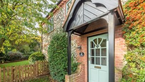 Una casa in mattoni con una porta verde, un piccolo portico e una recinzione in legno.