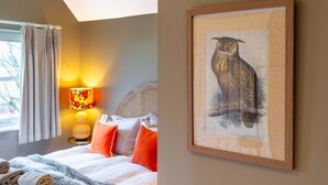 Una camera da letto con un letto, cuscini, una lampada e un quadro appeso al muro raffigurante un gufo.