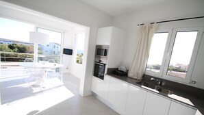 Een moderne keuken met witte kastjes, een ingebouwde oven en een groot raam met gordijnen.