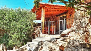A rustic stone building with a wooden porch and steps leading up to it, surrounded by greenery and rocks. - Santa Giulia Beach & Charming stone house (porto vecchio)