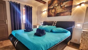 A bedroom with a bed, curtains, a painting, and a nightstand. - Santa Giulia Beach & Charming stone house (porto vecchio)