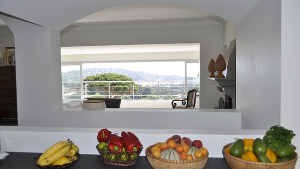 Une cuisine donnant sur un balcon, un coin repas avec une table, et divers fruits et légumes disposés sur le comptoir.