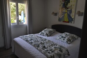 Een bed met een bloemenbedekking, een raam met gordijnen en een muur met een geometrisch schilderij.