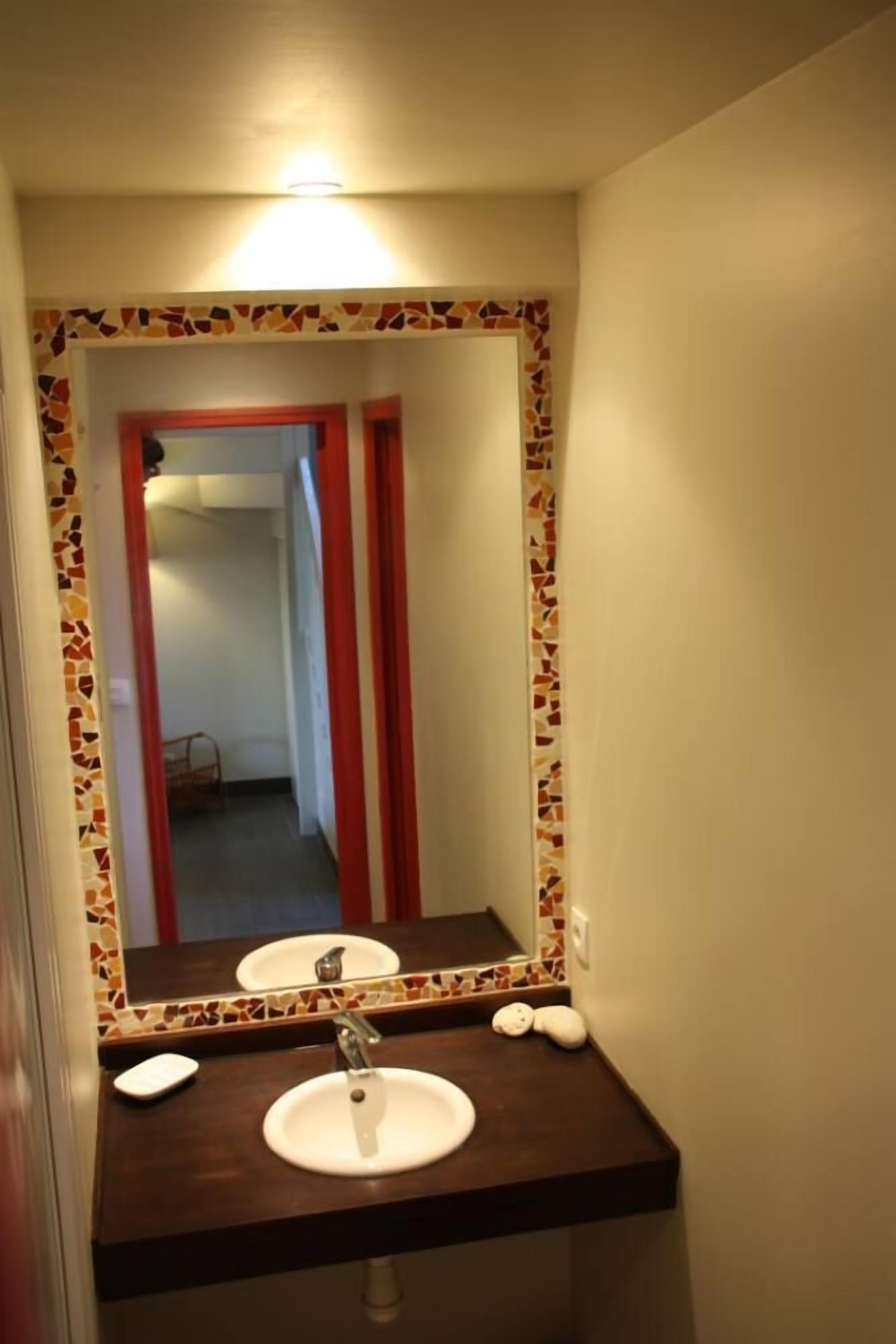 A bathroom with a tiled mosaic border, a white sink, and a mirror.