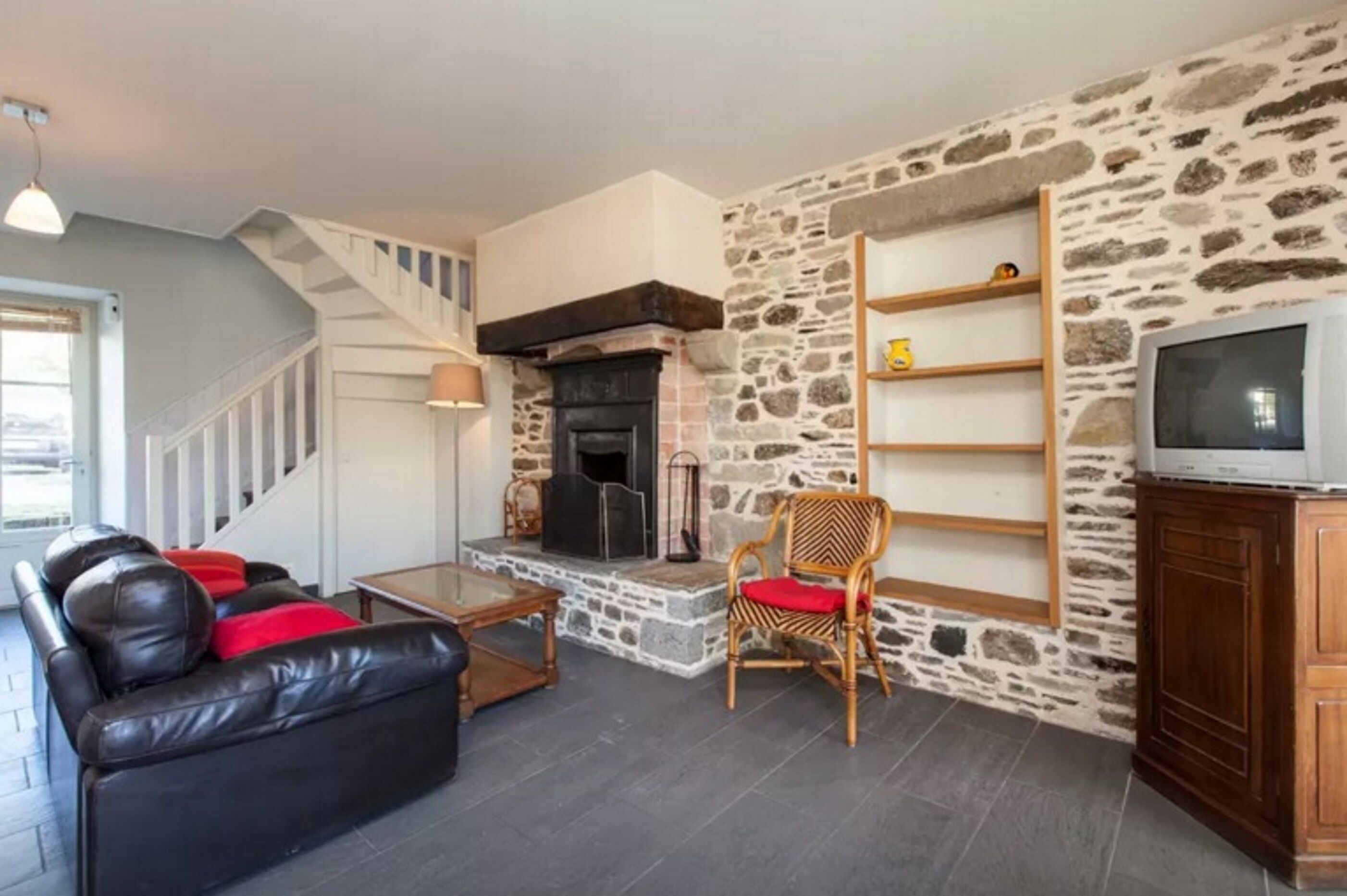 A living room with a stone wall, a fireplace, a sofa, a chair, and a television.