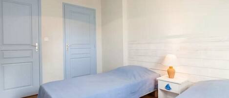 A room with two single beds, a white nightstand with a lamp, and a wooden floor.