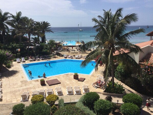 A pool area with lounge chairs, palm trees, and a view of the ocean.