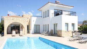 Una casa moderna de dos pisos con piscina, un arco de piedra y varias sillas de descanso.