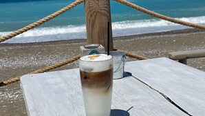 Una mesa de madera con un vaso de café helado, cuerdas y un poste de madera con piedras en la playa.