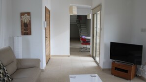 A living room with a sofa, a flat-screen TV on a wooden stand, a painting on the wall, and a staircase leading to another room.