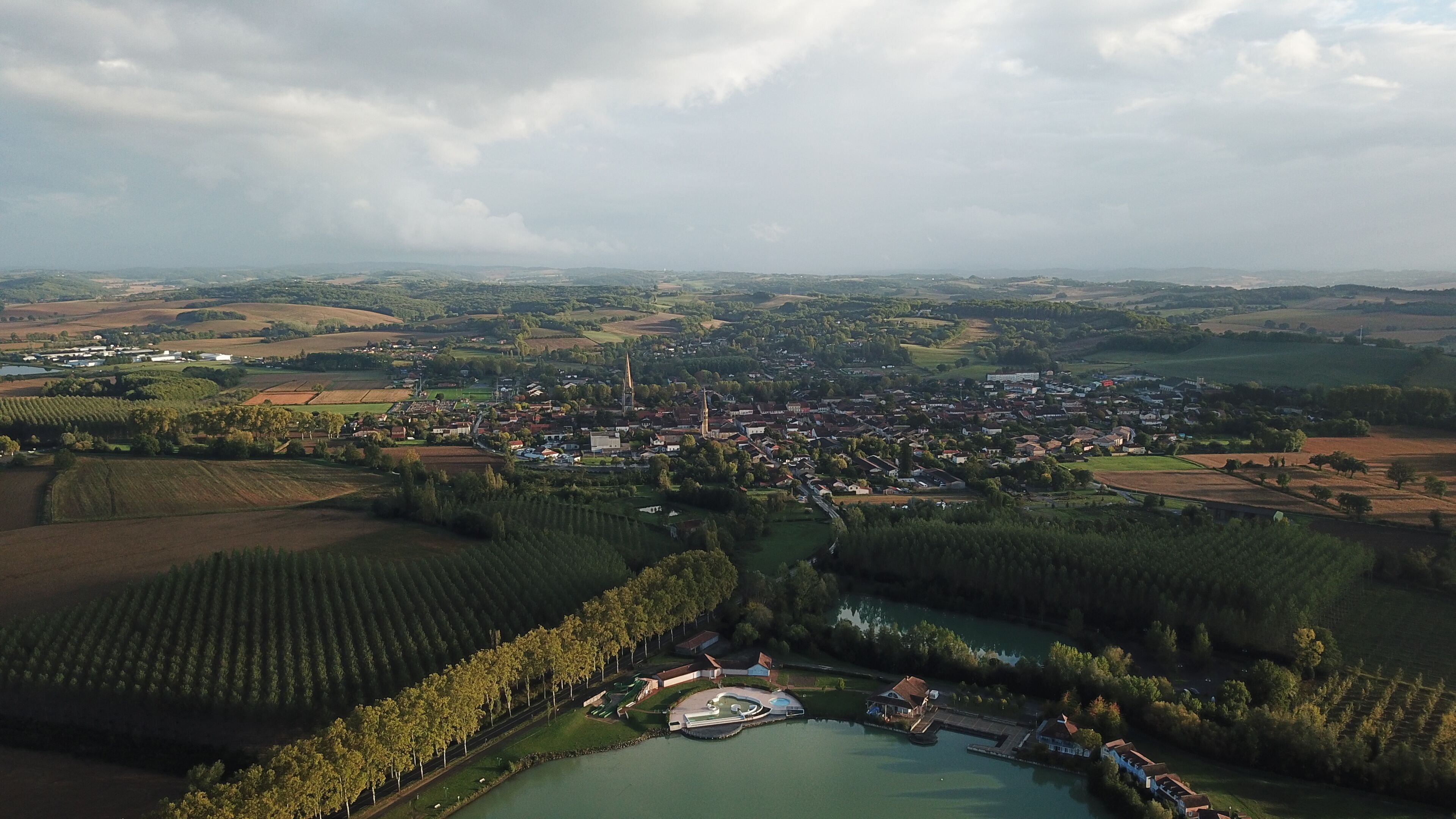 Vista aérea de un pueblo con una iglesia destacada, un lago y campos agrícolas circundantes.