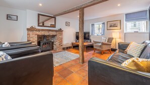 A cozy living room with a brick fireplace, leather sofas, a wooden beam ceiling, and a television. - Algerine Cottage,  Wells-next-the-Sea, Norfolk (Wells-next-the-Sea)