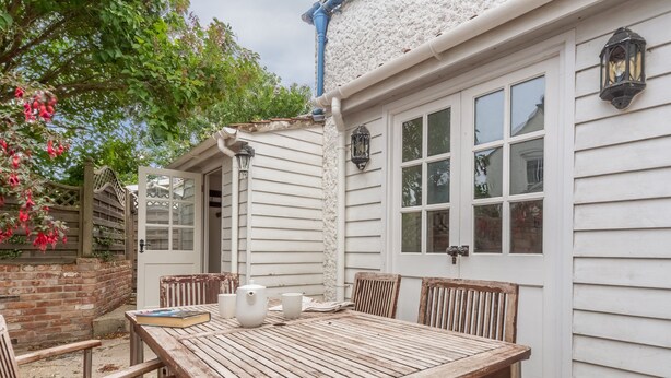 A wooden table with chairs, a white door, and a brick wall. - Algerine Cottage,  Wells-next-the-Sea, Norfolk (Wells-next-the-Sea)
