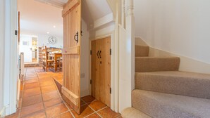 A staircase leading to a second floor, a wooden door, and a kitchen area with a clock. - Algerine Cottage,  Wells-next-the-Sea, Norfolk (Wells-next-the-Sea)