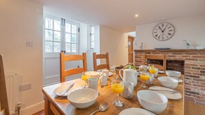 A dining area with a wooden table set for breakfast, including bowls, glasses of orange juice, and a clock on the wall. - Algerine Cottage,  Wells-next-the-Sea, Norfolk (Wells-next-the-Sea)