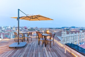 A rooftop terrace with wooden flooring, tables, chairs, and a large umbrella.