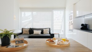 Un soggiorno moderno con un divano, un tavolino da caffè con cose per la colazione e un angolo cottura con macchina del caffè.