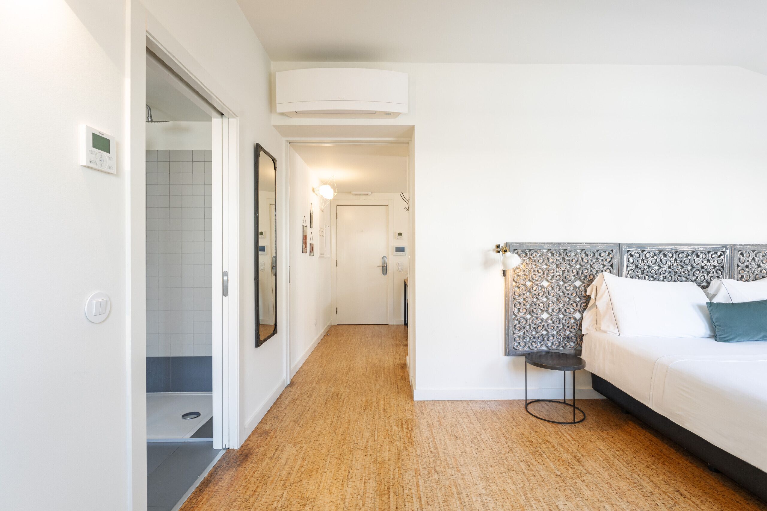 Een hotelkamer met een houten vloer, een bed met een gestreept hoofdeinde, een nachtkastje en een spiegel aan de muur.