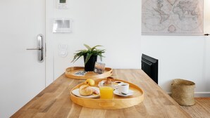 Un vassoio della colazione con croissant, un bicchiere di succo d'arancia e una tazza di caffè su un tavolo di legno in una stanza con una porta bianca, un termostato, una pianta in vaso e una mappa del mondo appesa al muro.