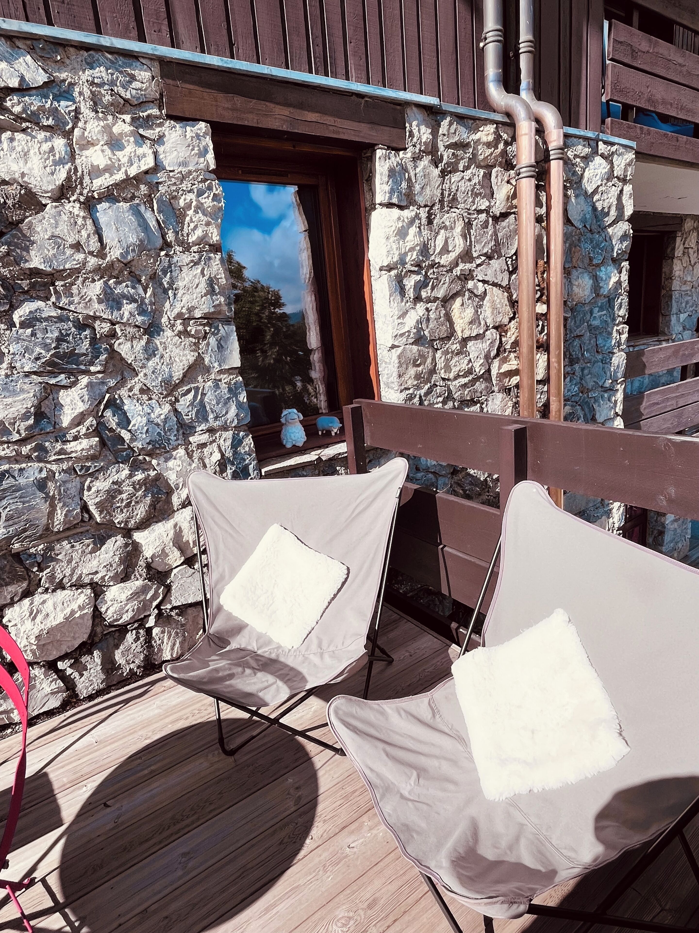 A wooden deck with two cushioned chairs, a stone wall, and a wooden railing.