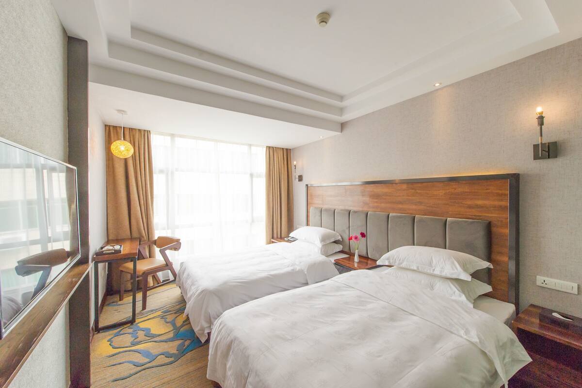 Habitación de hotel con dos camas, un escritorio, una silla, un televisor y una ventana con cortinas.