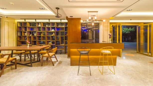 A modern interior with a long dining table, bar stools, and a bookshelf filled with decorative items.