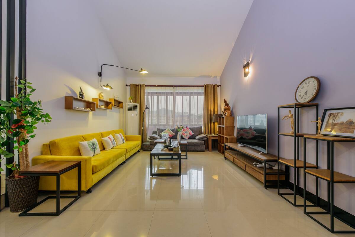 Una sala de estar moderna con un sofá amarillo, una mesa de centro y un televisor sobre un mueble de madera.