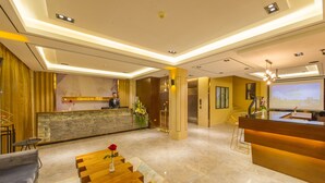 A modern hotel lobby with a reception desk, seating area, and a large screen displaying a cityscape.
